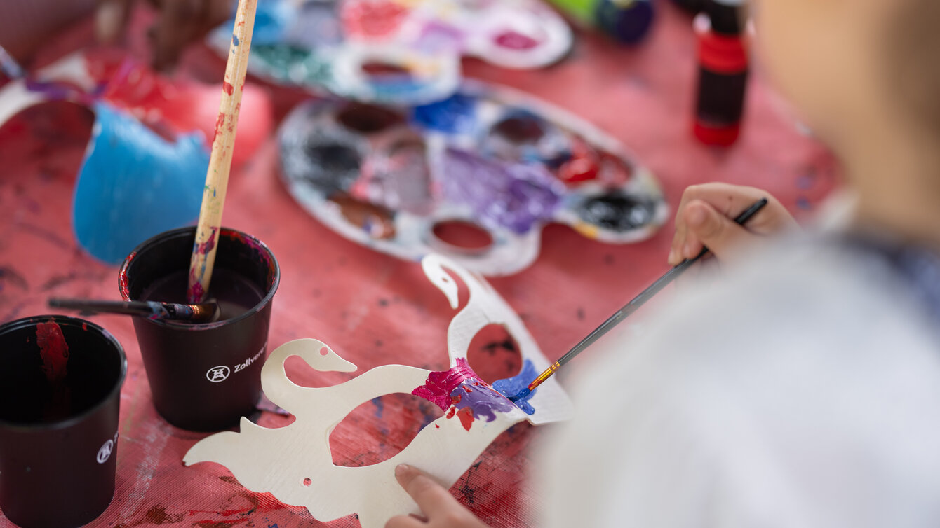 Ein Kind bemalt eine Maske mit bunten Farben.
