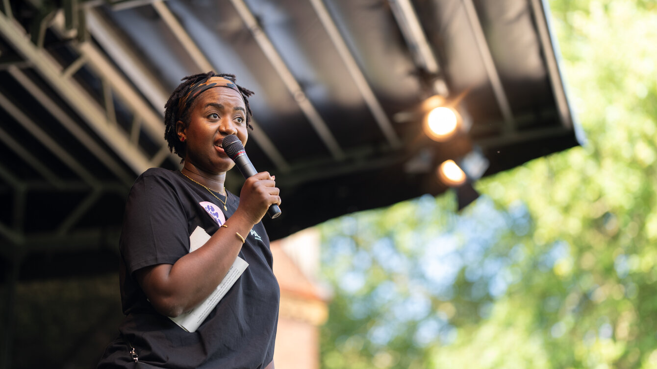 Eine Person steht auf einer Bühne und spricht in ein Mikrofon.