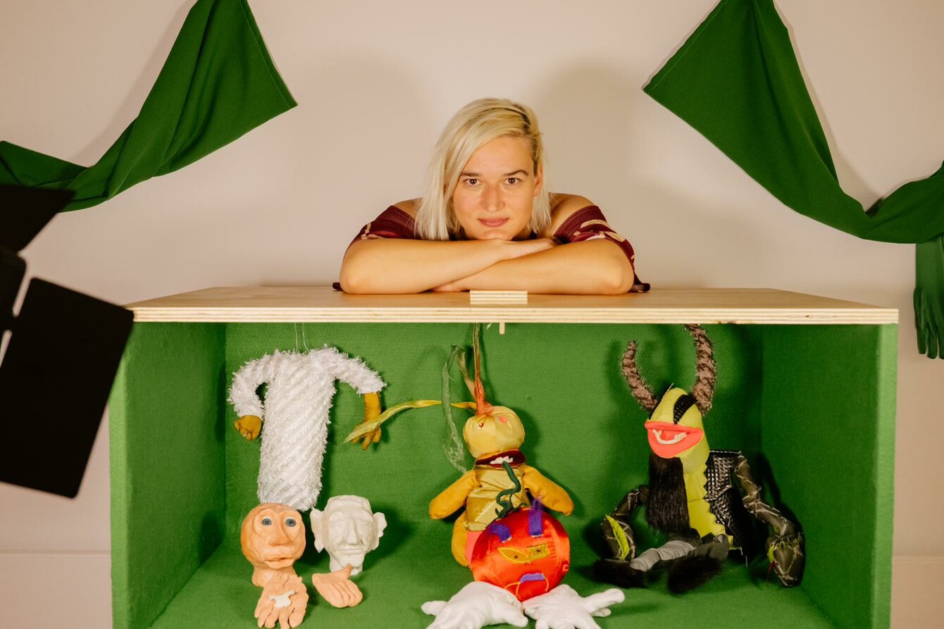 Maru Mushtrieva einer einem Puppenspielkasten, welcher mit einem Green-Screen ausgekleidet ist. Im inneren sind mehrere Figuren zu sehen.