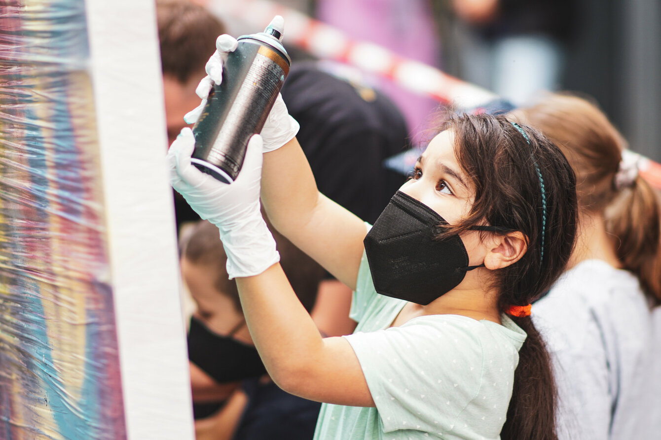 A child paints a canvas with a spray can.