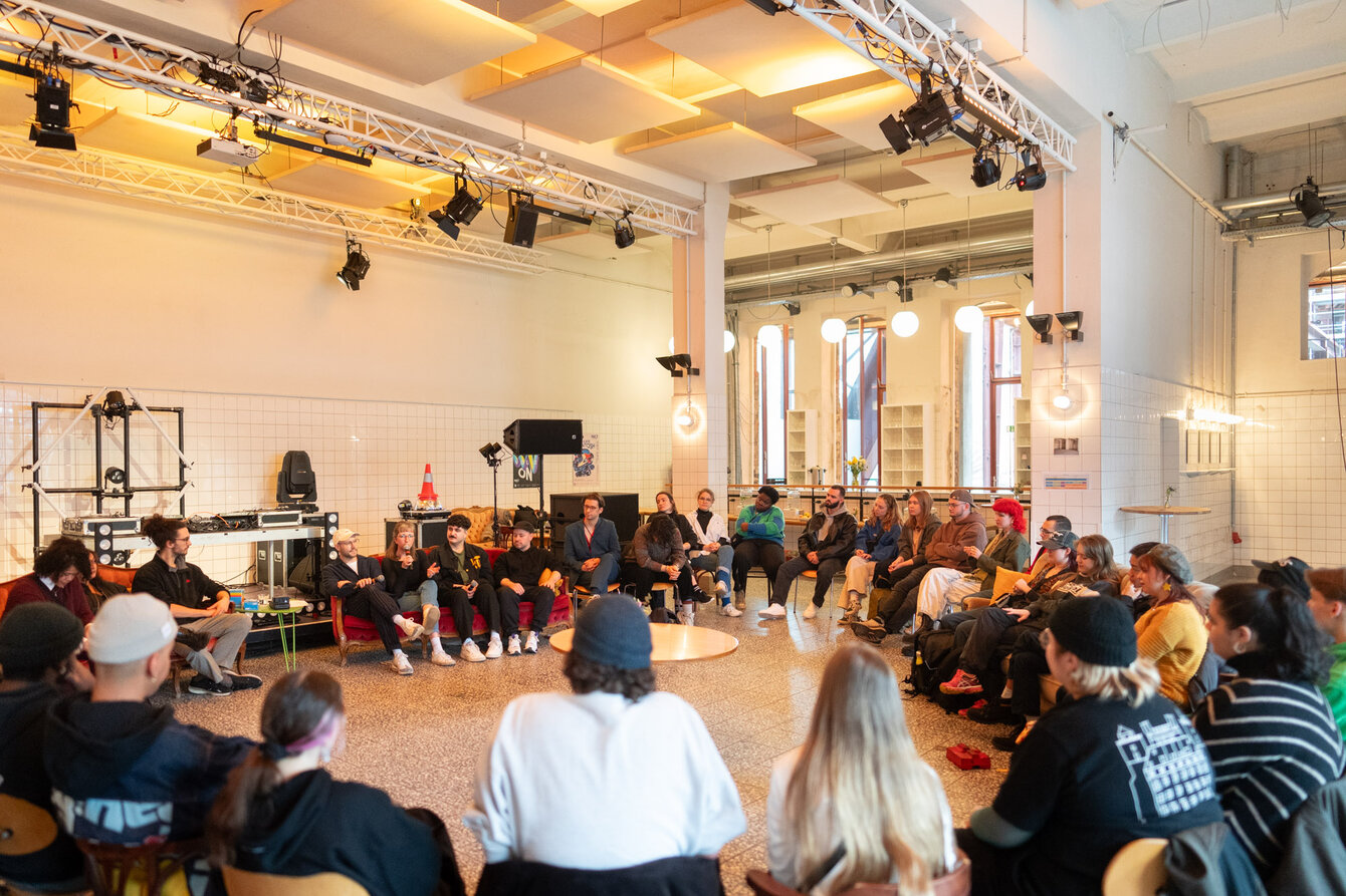 Eine Gruppe sitzt in einem großen Stuhlkreis im PACT Foyer zusammen