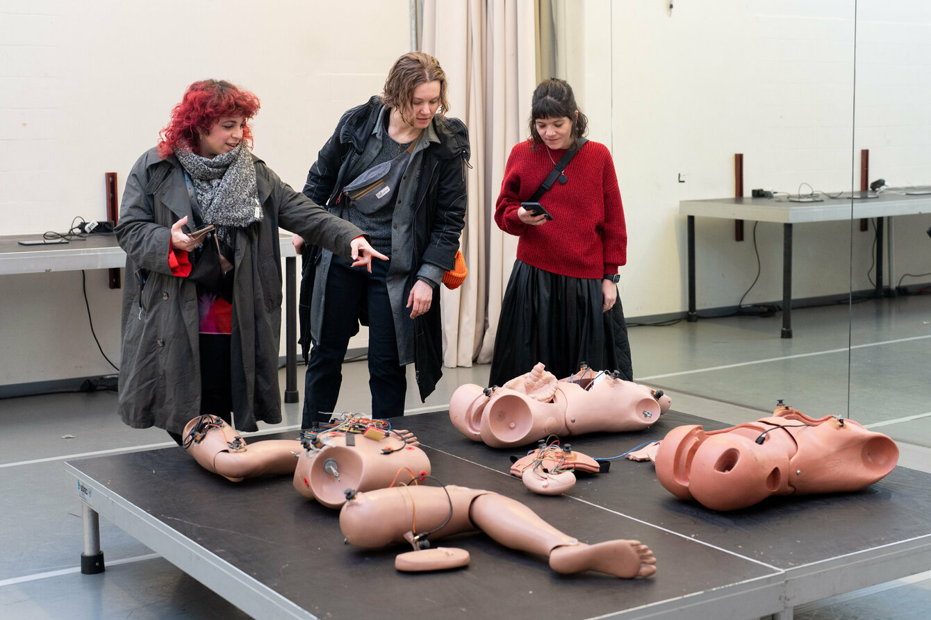 Drei Besucher:innen werden ins Innere geführt und zeigen auf einen Auflagetisch. Dort liegen Prothesen menschlicher Körperteile aus, in die Robotertechnik eingesetzt wurde. 