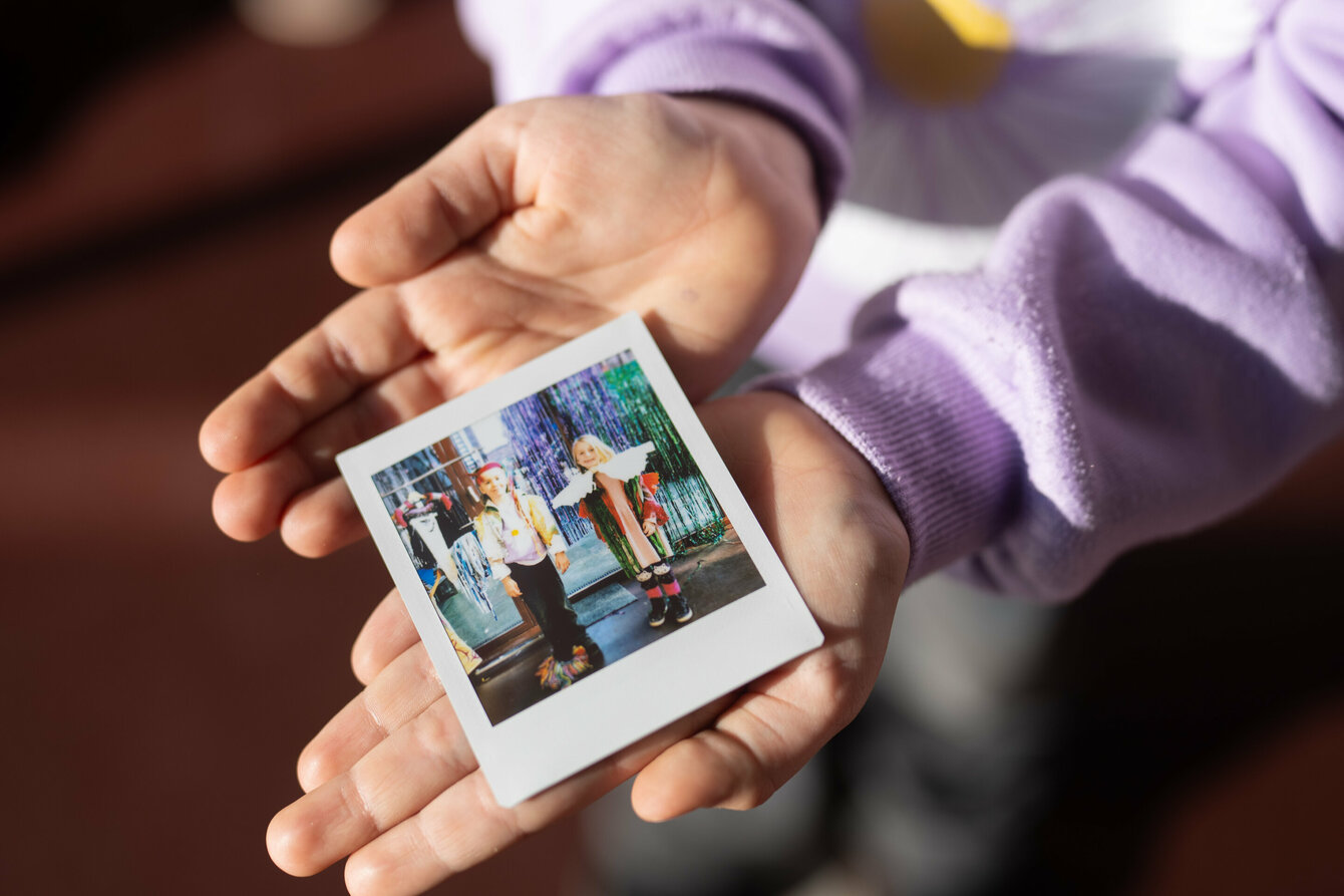 Ein Kind hält ein Polaroid-Foto in der Hand. Auf dem Foto sind zwei Kinder in bunter Verkleidung zu sehen.
