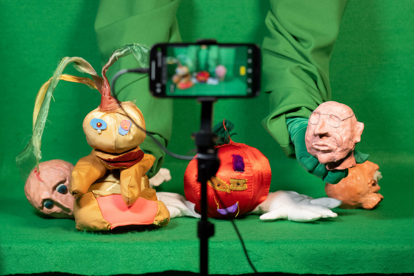 Verschieden Puppen und Figuren sind in einer Art Fotobox platziert, welche in grünen Stoff gehüllt ist.