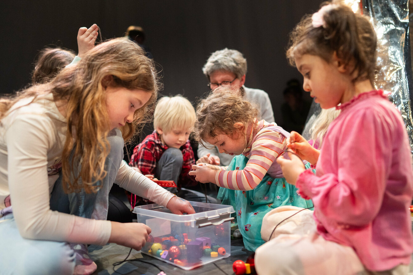 Kinder fädeln kleine Holzperlen auf einer Schnur auf