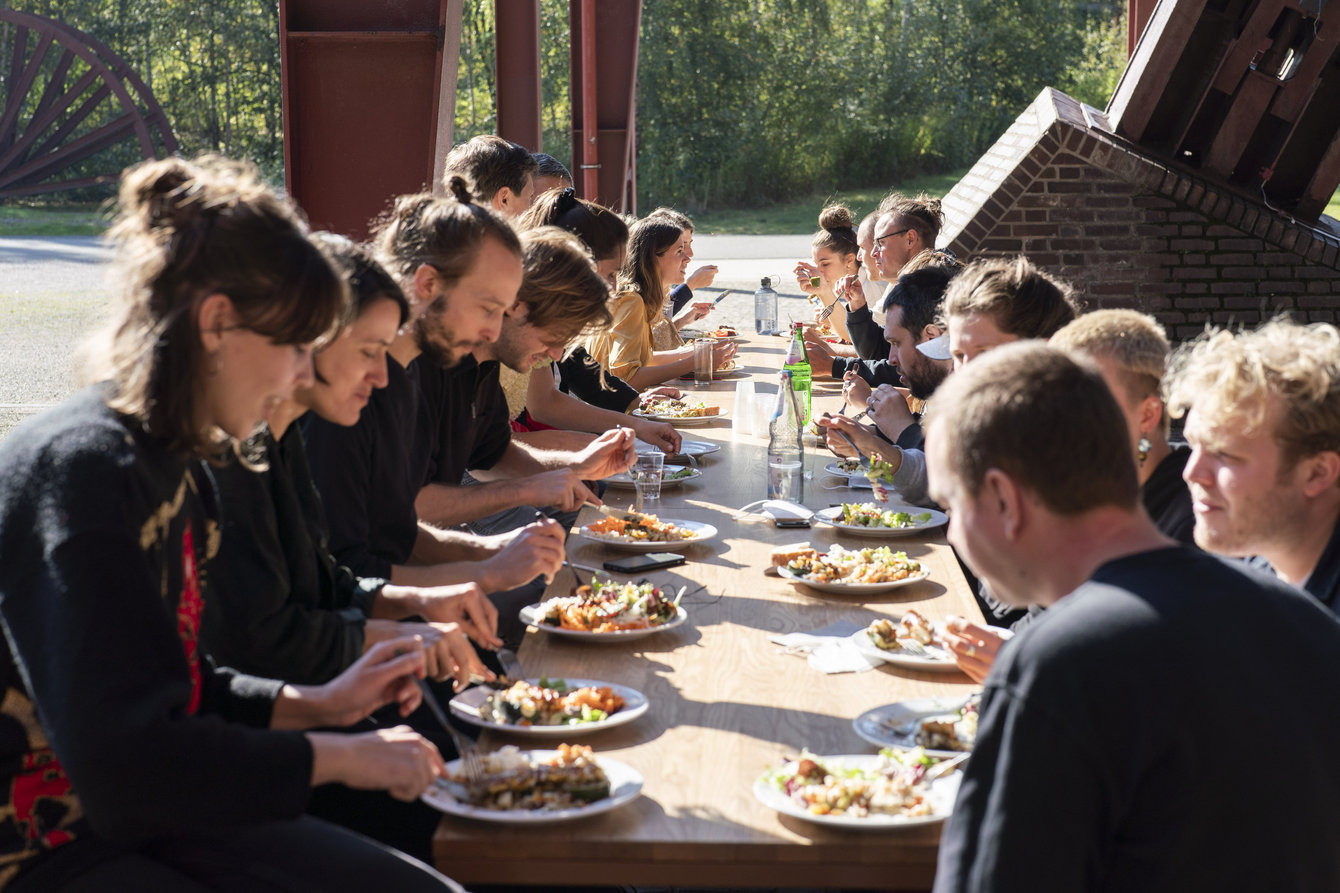 Eine Gruppe Menschen sitzt an einem langen Tisch vor PACT Zollverein