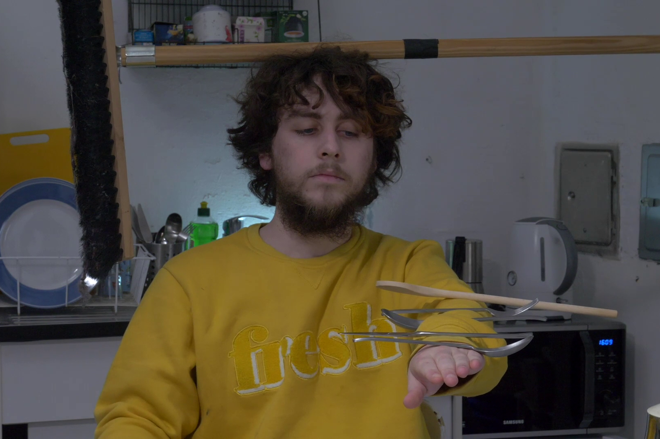 A young man balances high spoon and other utensils on his arm