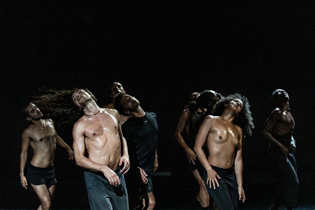 A scene from the performance F*cking Future: The image shows a group of dancers dancing shirtless on a darkened stage.