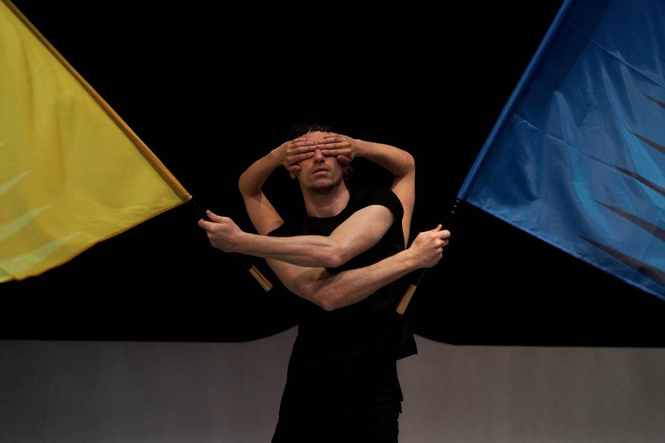 Tänzer:innen mit einer gelben und einer blauen Flagge auf der Bühne