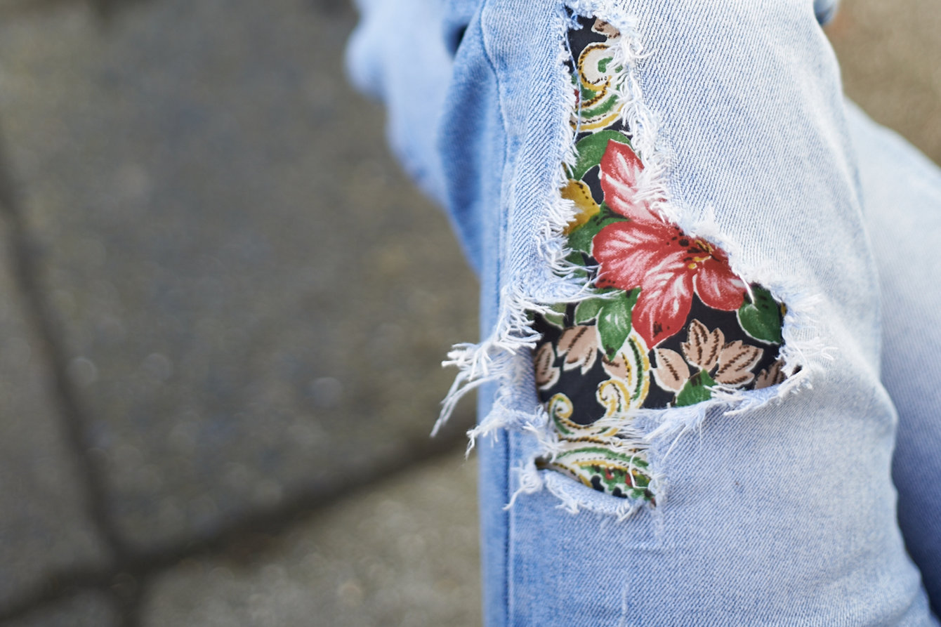 Eine kaputte Jean mit buntem Flicken mit Blumenmuster