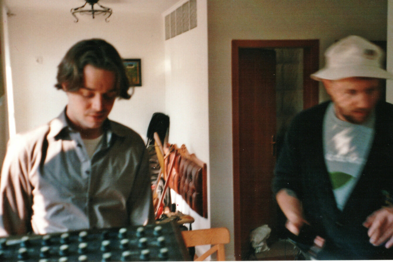 Ein Foto vom Berliner Duo Neuzeitliche Bodenbeläge. Das Foto ist leicht verschwommen und zeigt die beiden Mitglieder des Duos nebeneinander in einem Raum stehen. 