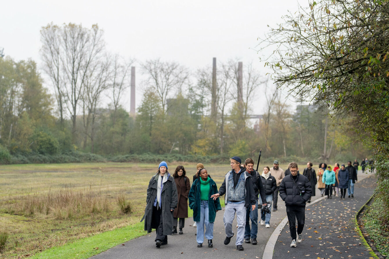 Eine Personengruppe geht auf einem Weg im grünen Spazieren. Die Gruppe läuft auf die Kamera zu.