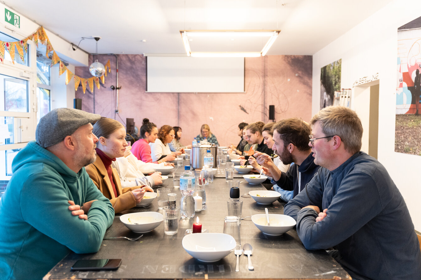 Eine Gruppe von Menschen sitzt an einer langen Tafel und isst gemeinsam 