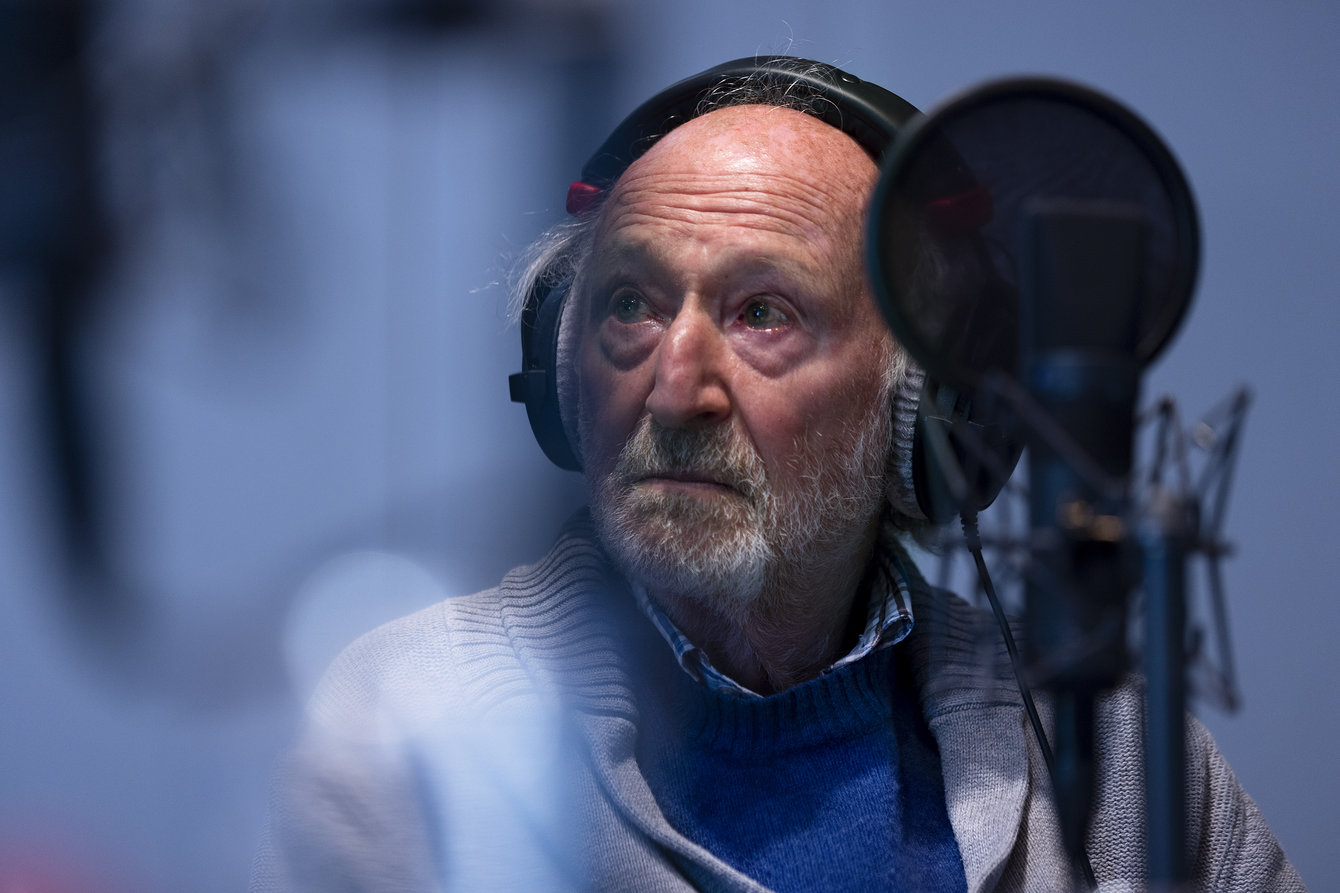 Ein älterer Herr mit Kopfhörern sitzt vor einem Mikro in einem Tonstudio und schaut auf einen nicht sichtbare Person