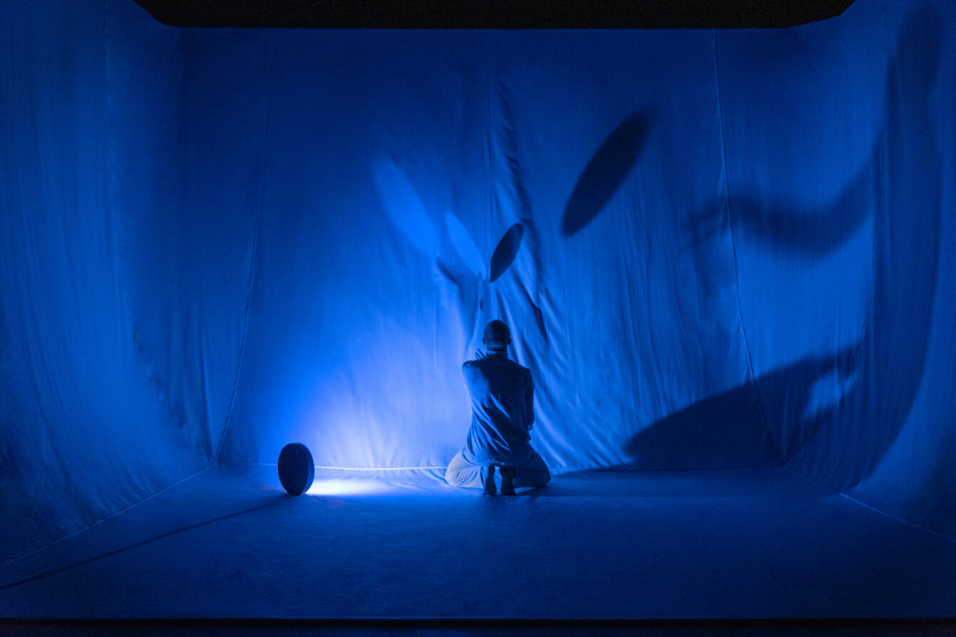Blaue Bühne mit Tüchern und einer Person die mit Scheiben jongliert