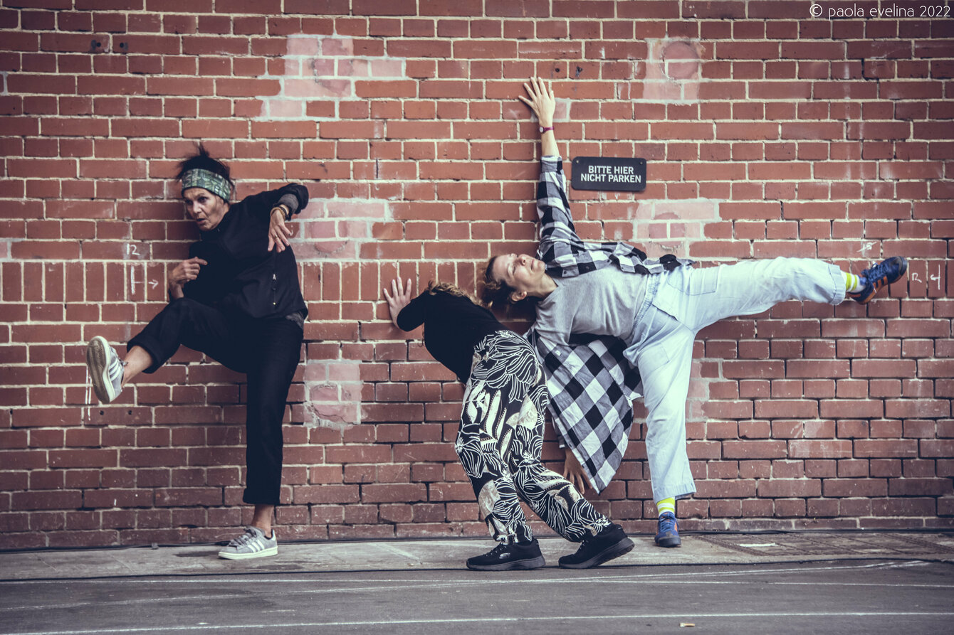 Drei Personen lehenn mit tanzenden Psoen an einer gemauerten Backsteinwand