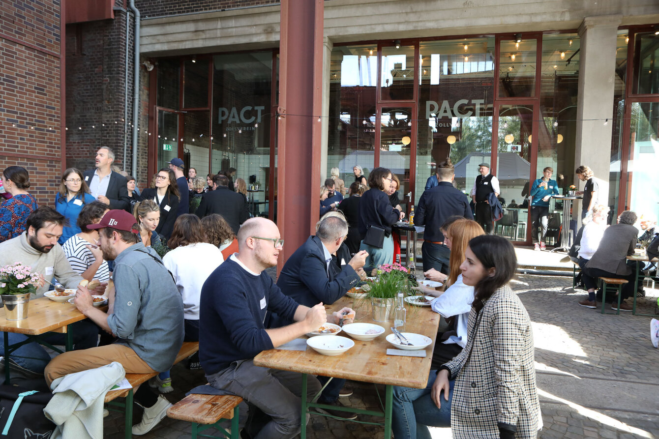 In front of the winter garden at PACT Zollverein, people are having lunch while the sun is shining 