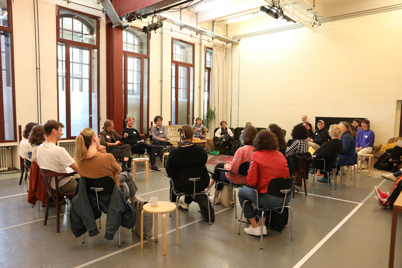 A group of people sit together in a circle of chairs to talk