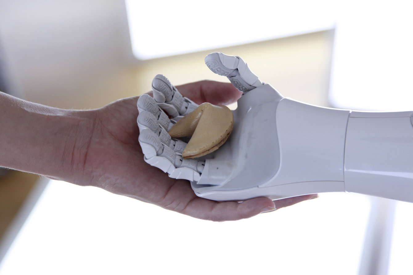 Roboter und Mensch Hand in Hand; gemeinsam halten sie einen Glückskeks