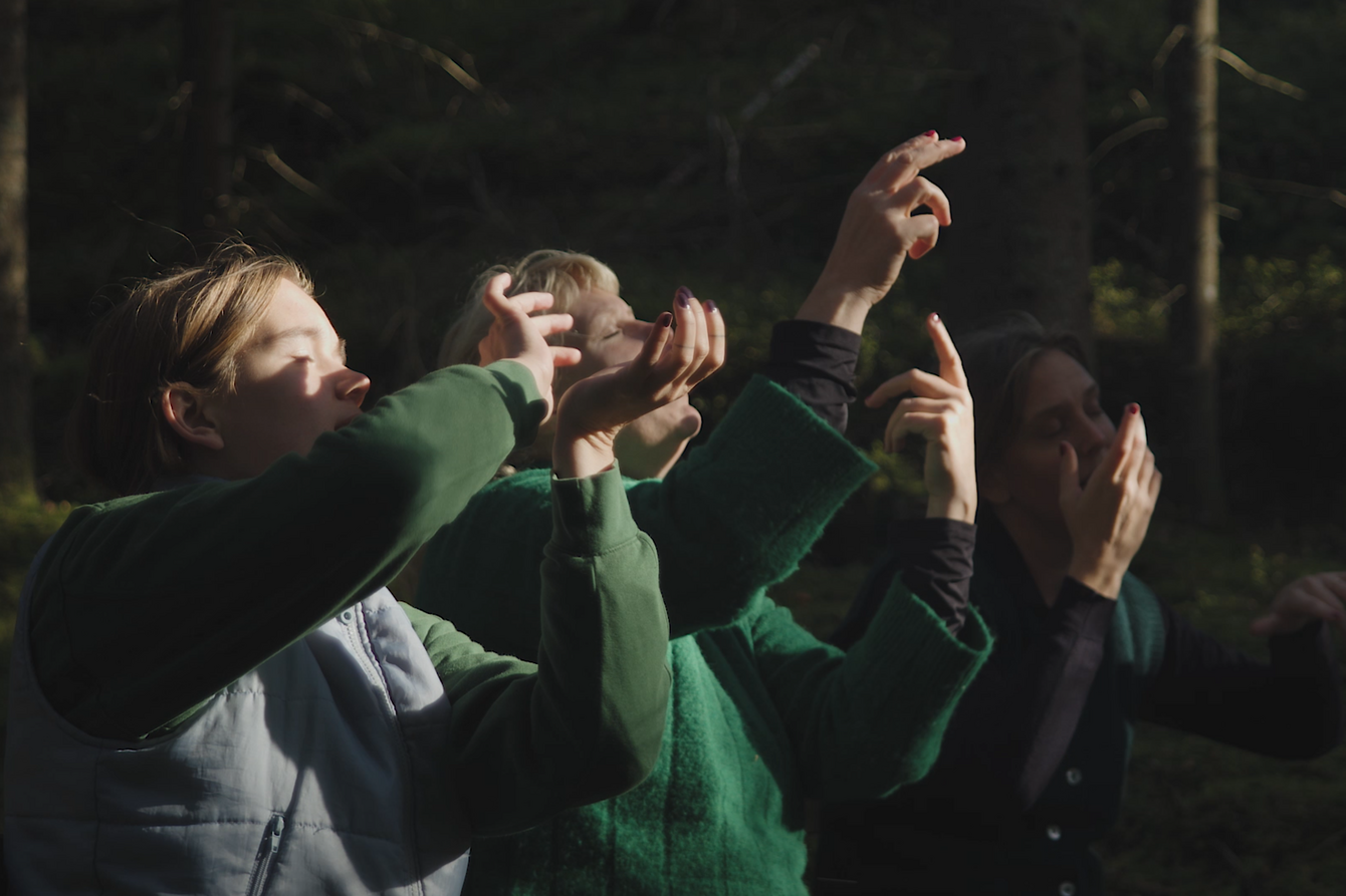 Drei Frauen sitzen in einem Wald un bewegen ihre Hände