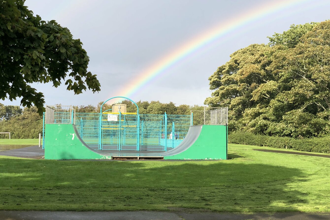 Foto von einer Skateanlage im Grünen über die ein Regenbogen scheint