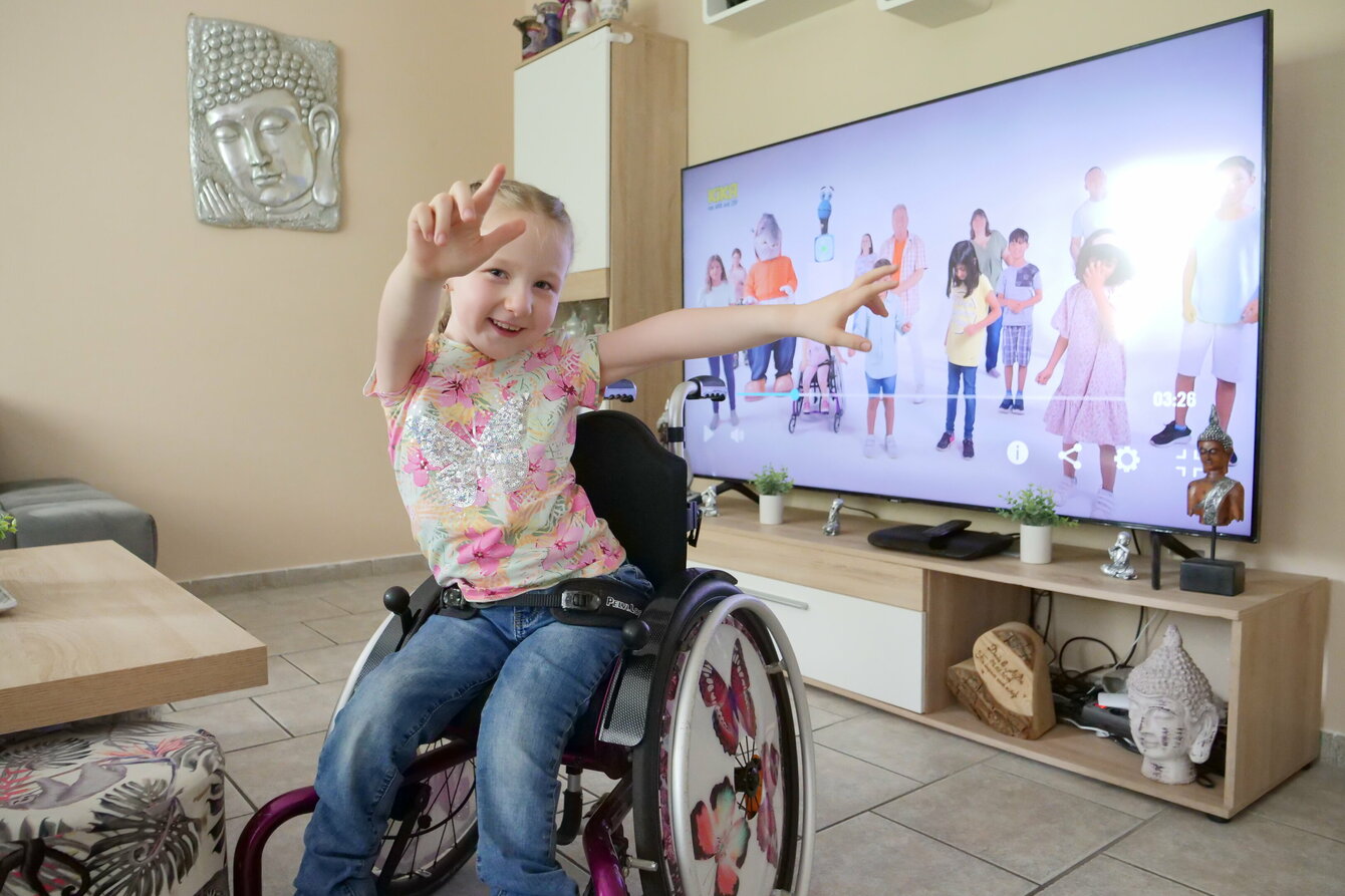 Ein junge Mädchen sitzt in einem Rollstuhl und reckt die Hände die Höhe