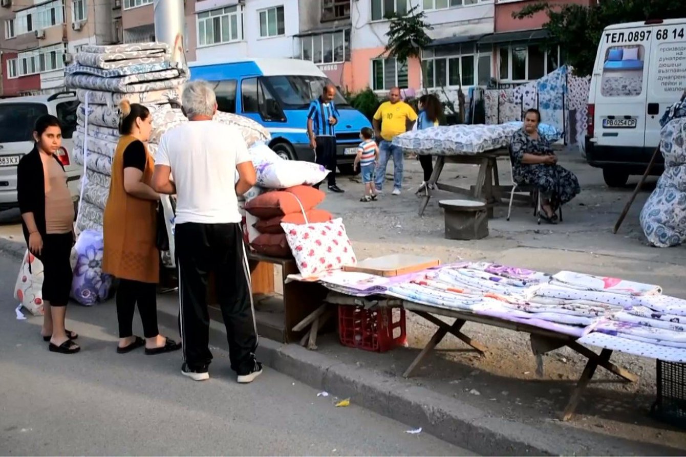 Drei Personen vor einem Stand mit Stoffen und Kissen 