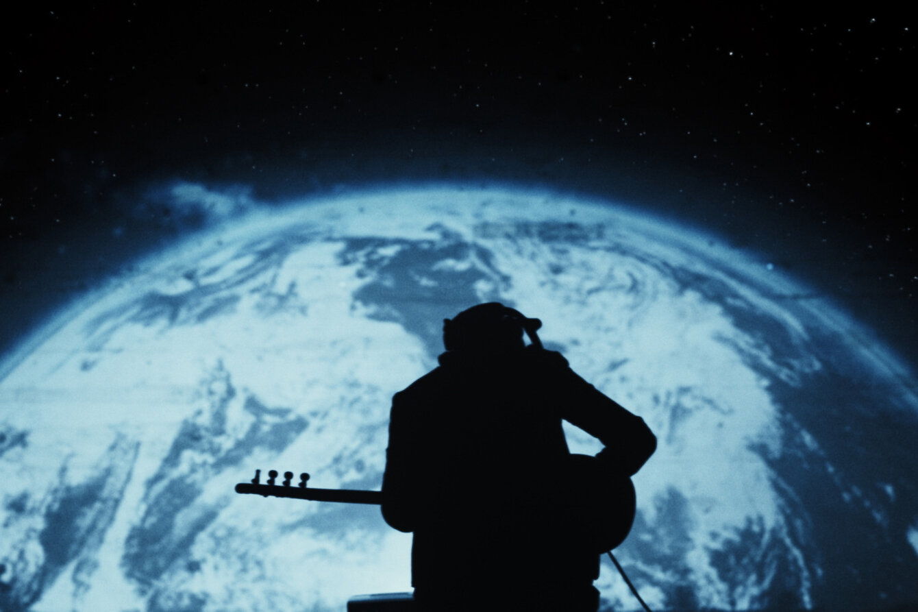 Ansicht von hinten einer Gitarre spielen Person vor einer projizierten Weltkugel