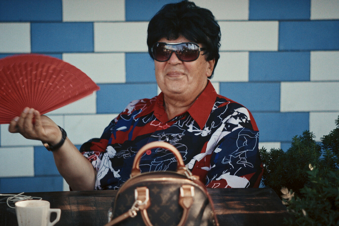 Eine Person einem bunten Hemd, Sonnenbrille und rotem Fächer