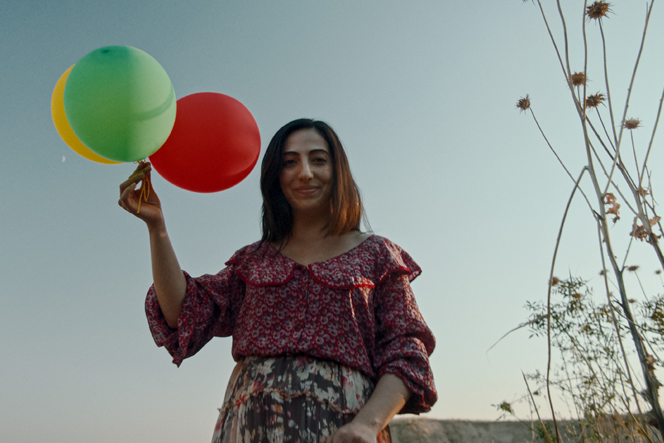 Eine Frau lächelt mit einem Strauß Luftaballons in der Hand in die Kamera im Film Nachbarn
