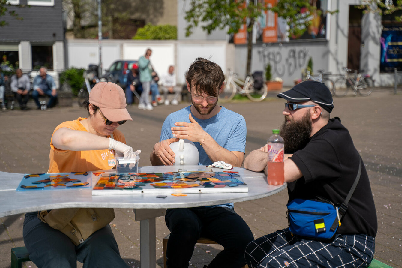 Menschen sitzen an einem Tisch und legen bunte Mosaike