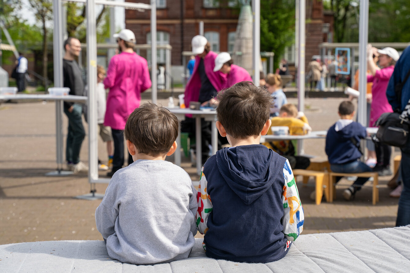 Kinder sitzen mit dem Rücken zur Kamera und beobachten das bunte Treiben auf dem Katernberger Markt