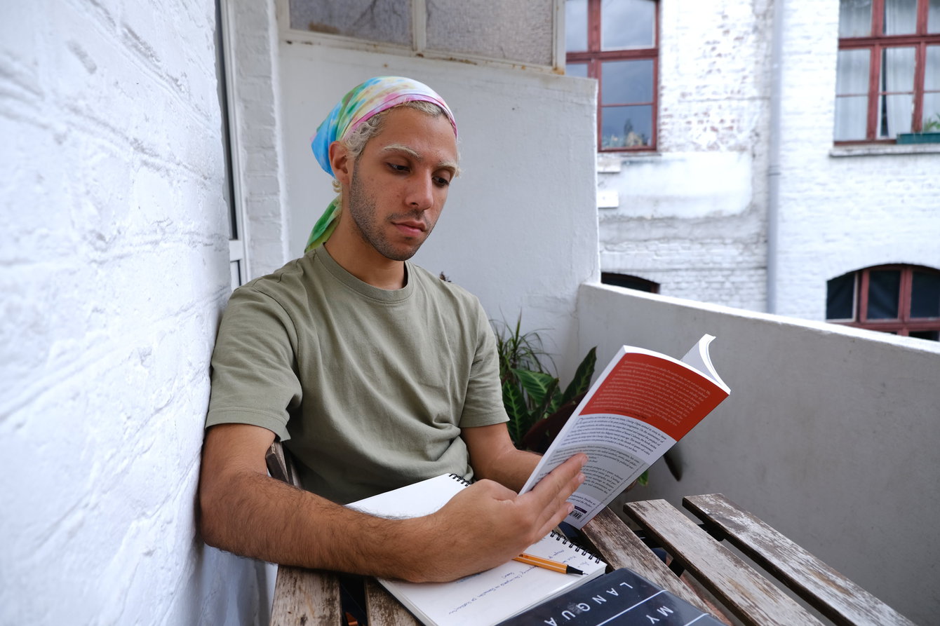 Igor Meneses reads ›Cruising Utopia‹ by José Estaban Munoz at their apartment's balcony. 