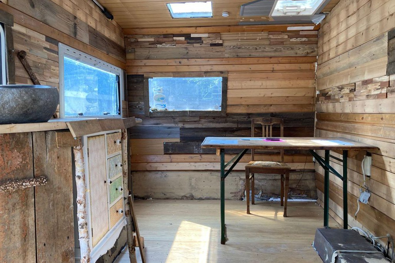 Sicht in einen Campervan, komplett mit Holz ausgekleidet, ein Tisch, Stuhl. 