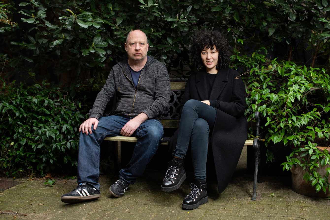 Tim Etchells & Aisha Orazbayeva auf einer Bank im Grünen