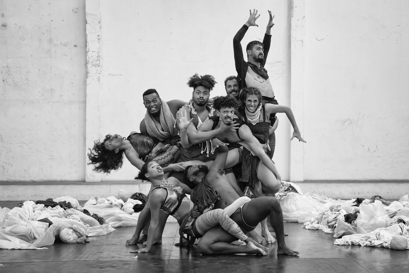 A group photo of the performers of the play “BORDA” in black and white. They form a group standing close together and looking into the camera with expressive facial expressions. 