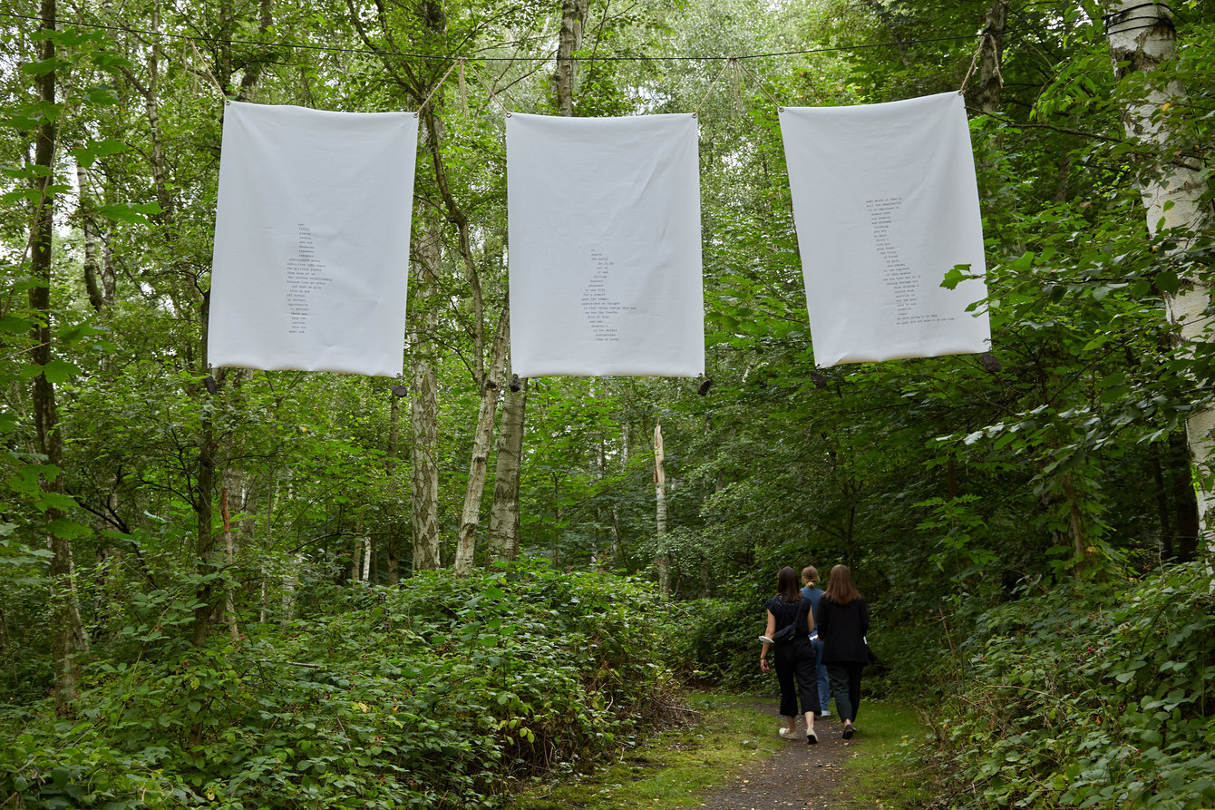 Drei Banner mit Botschaften hängen zwischen Bäumen über einem Waldweg