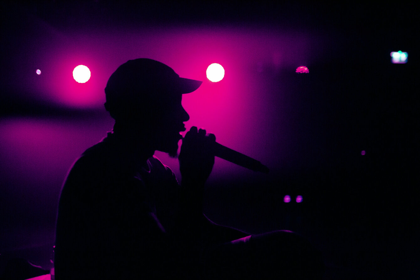 Ein dunkler Schatten vor buntem Licht auf einer Bühne mit Mikrofon in der Hand