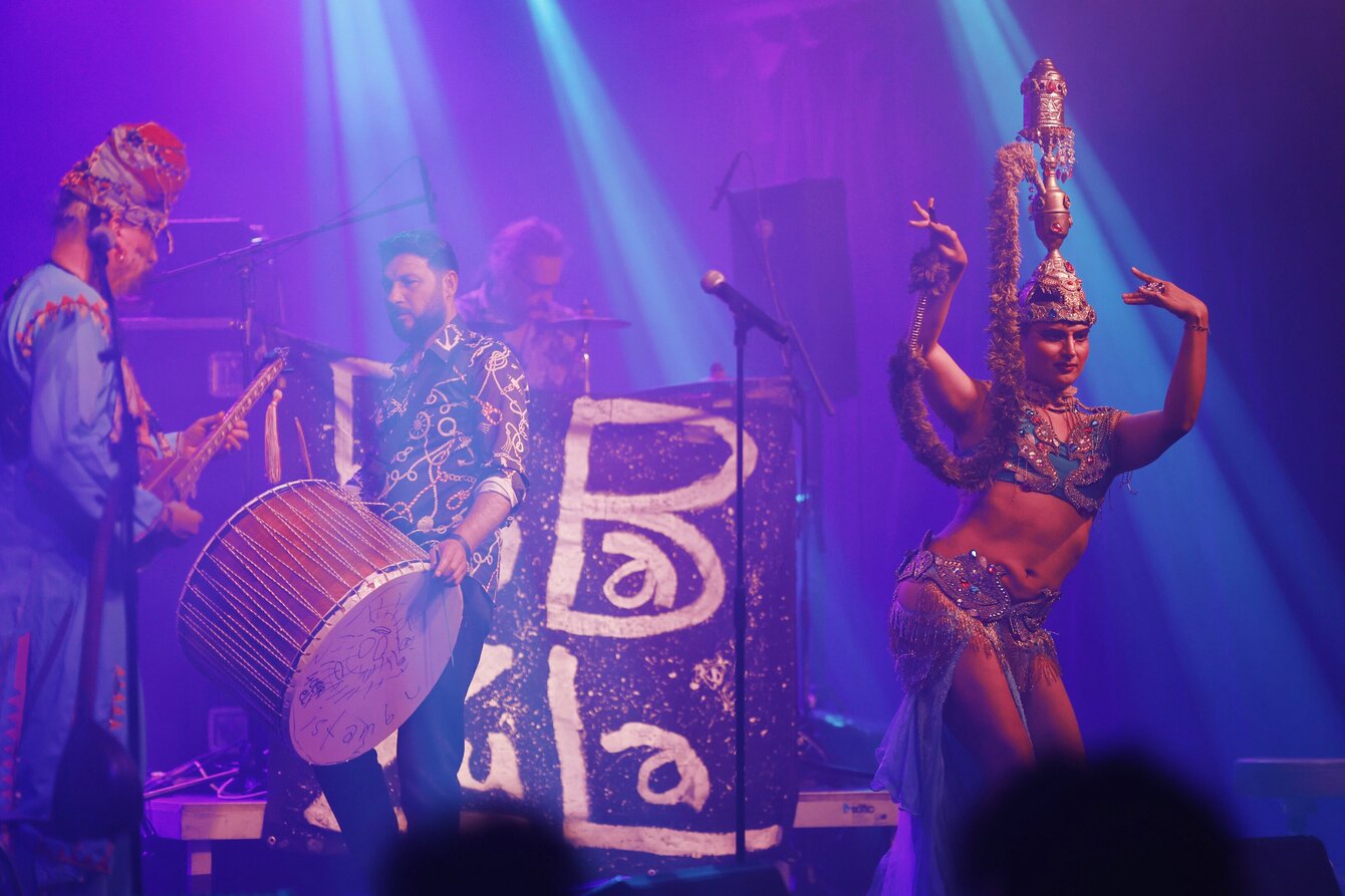 Eine Konzertsituation. Auf der Bühne sind Baba Zula zu sehen sowie Prince Emrah beim Performen. 