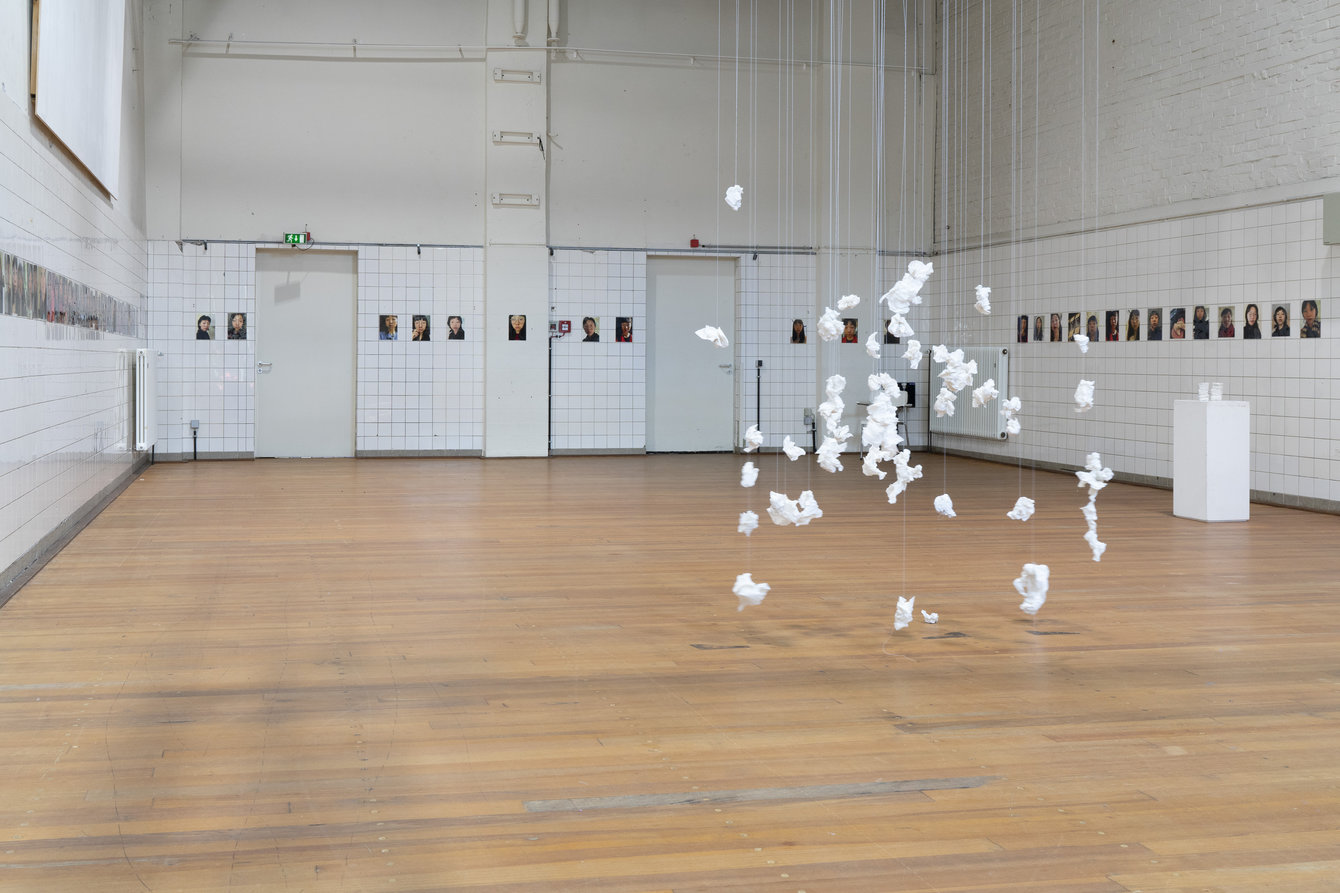 Komplette Raumansicht. Portraitbilder hängen an der Wand, zerknülltes Papier von der Decke. 