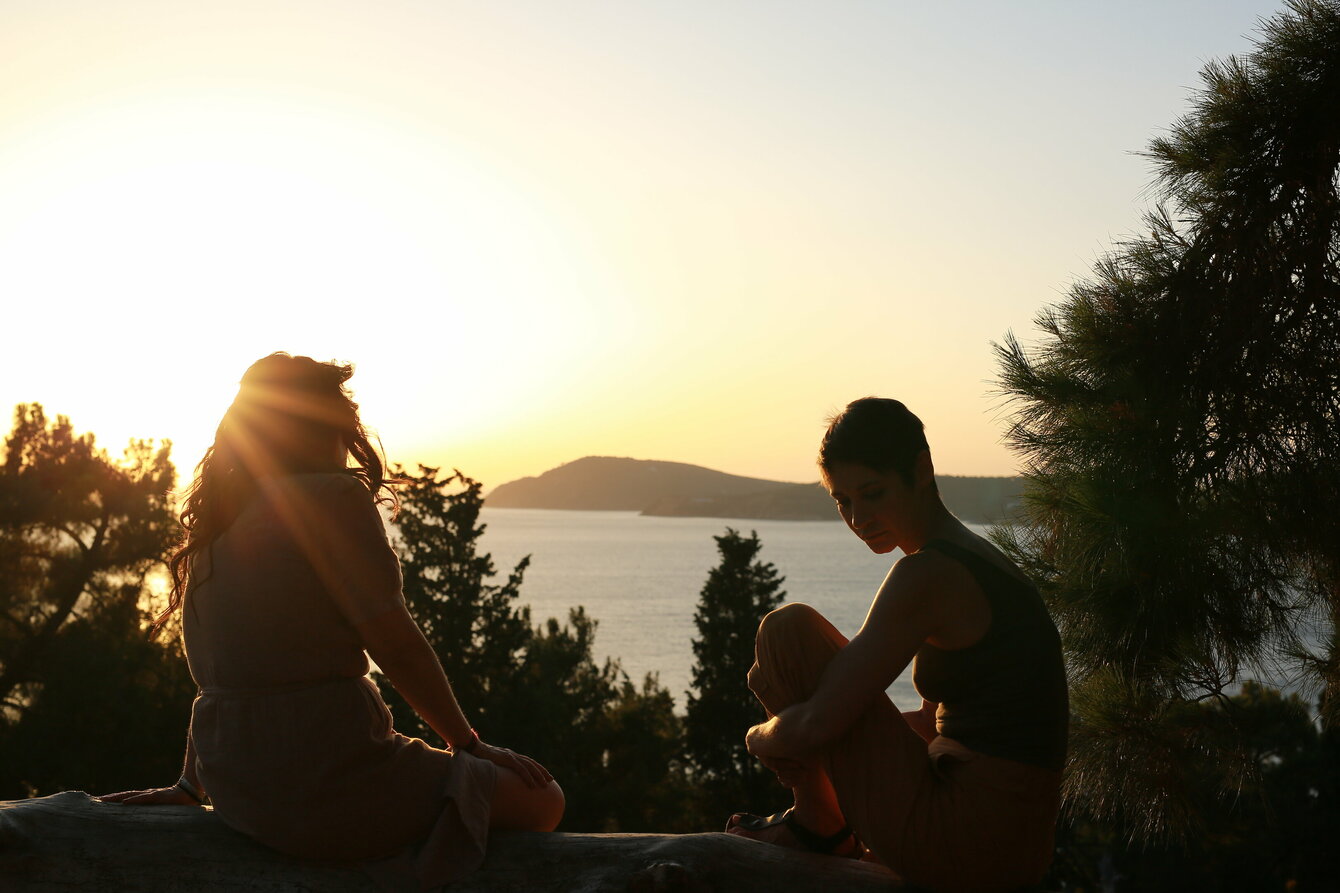 Zwei Frauen sitzen auf einer halbhohen Mauer und Blicke in den Sonnenuntergang