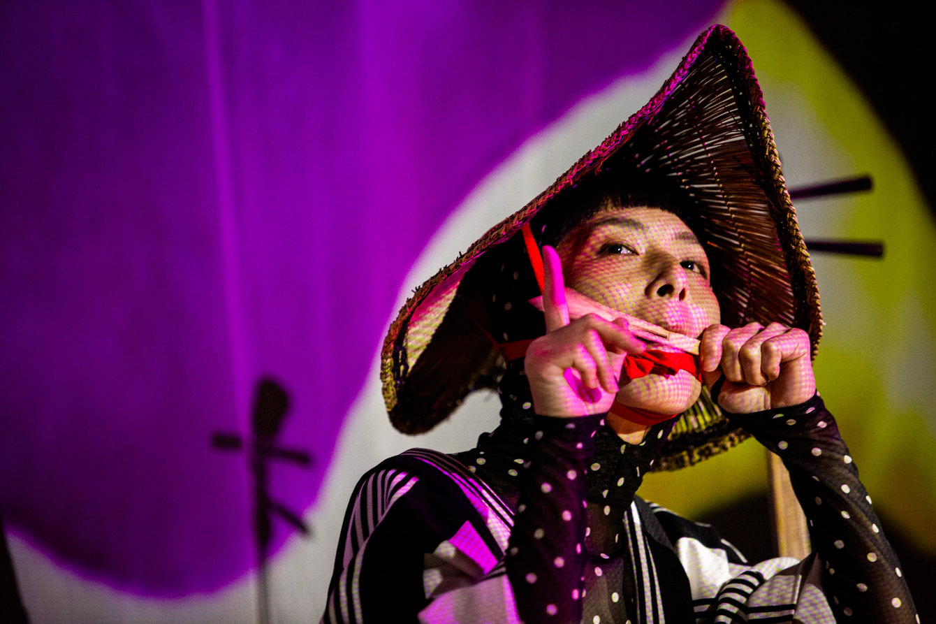 Tsubasa Hori plays Japanese instruments like the Taiko drum and Shamisenand sings in a circular setup. The public takes place in this arena-like settingwhile video projections appear on the curtains