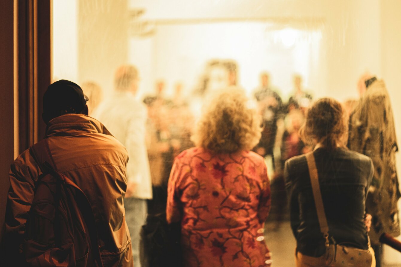 Eine Menschengruppe betrachtet abends Kunst in einem Ausstellungsraum.