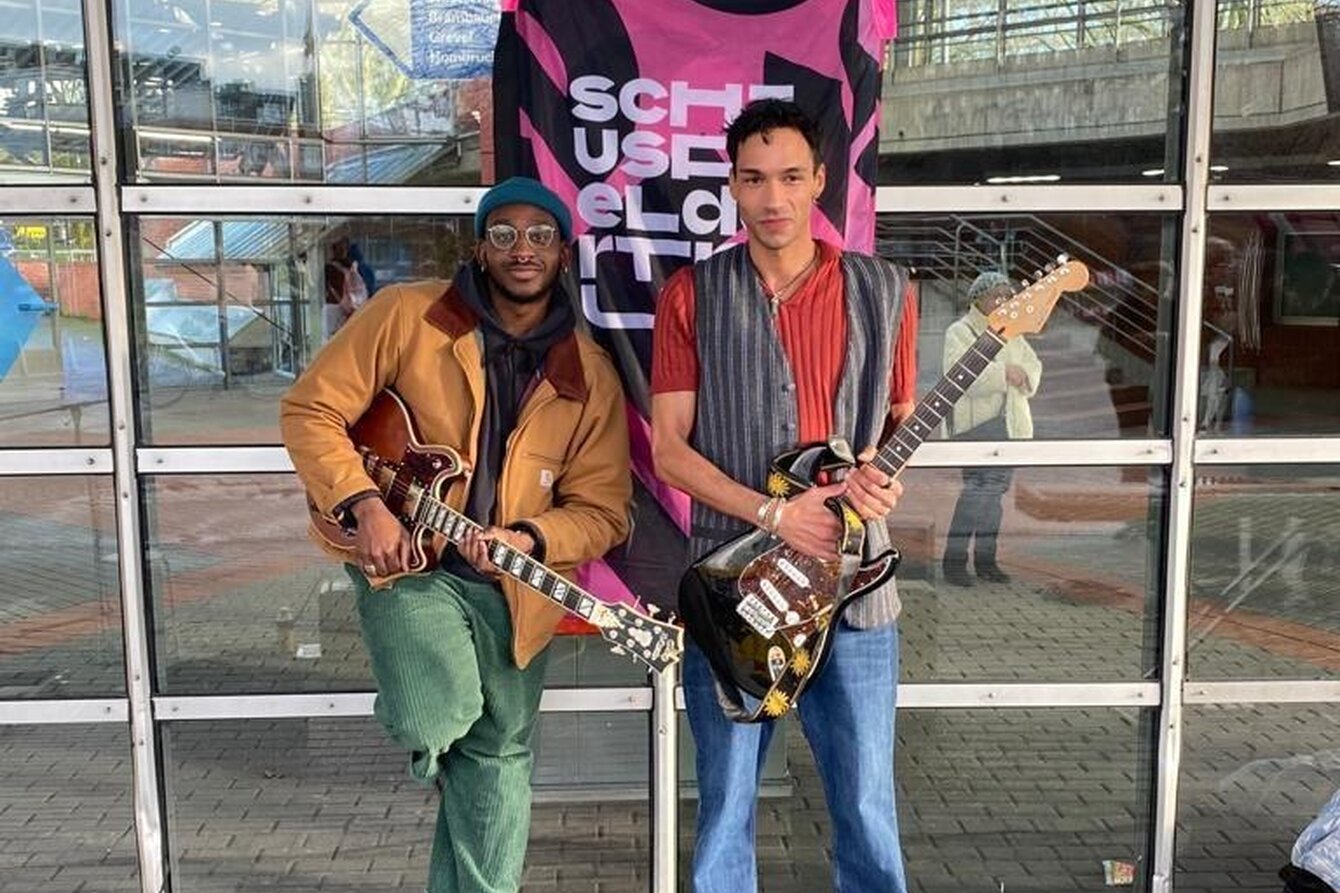 Joel und Salah stehen mit Instrumenten in der Hand vor einer Wand