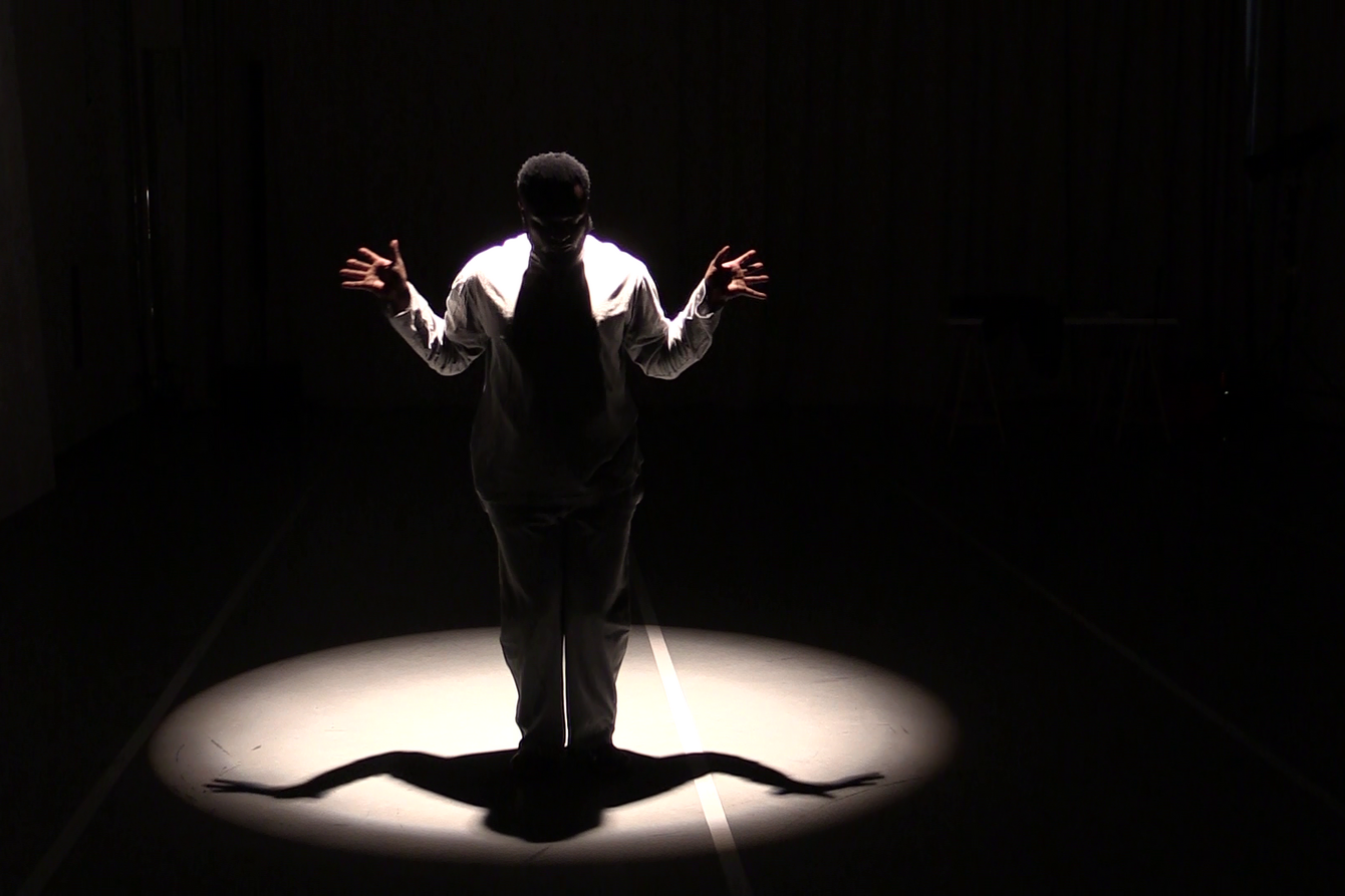 Koloto Siraji in einem weißen Anzug auf einer schwarzen Bühne im Lichtkegel
