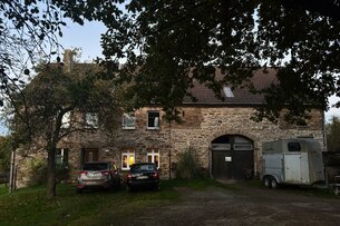 A big house on the country side in Germany with visible stones on the facade. The photograph is taken in the evening light, picturing the front, framed by trees.