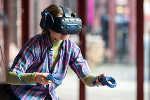 One person has put on VR goggles and is holding two controllers in their hands. 