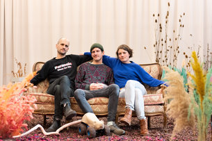 Daniel Ernesto Müller, Simon Hartmann sitzen auf einem Sofa in ihrem Bühnenbild bestehend aus bunten Trockenpflanzen, in ihrer Residenz im PACT Studio 