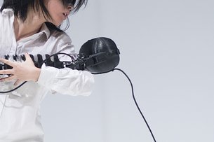 Eine Person hält einen dunklen Kopfhörer im Arm. Die Haltung erinnert an das Wiegen einen kleinen Babys. 