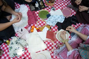 A group of people sitting comfy on the floor. They are all stitching and sewing independently their own.  